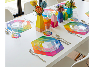 A dining table place setting with an artist-designed paper placemat, plate, fork, knife, and water glass